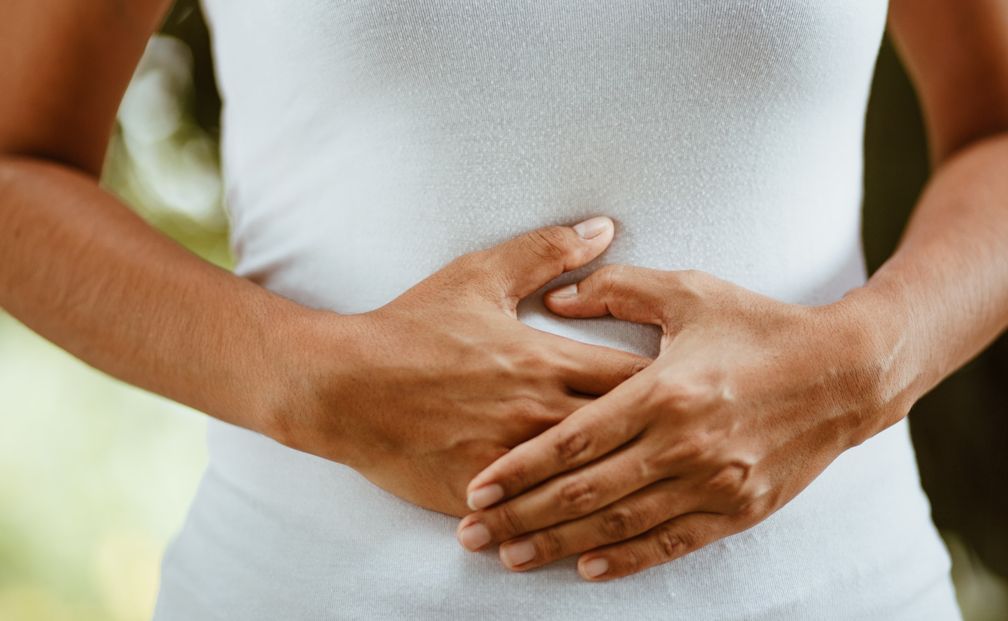 Eine Frau in einem weißen, eng anliegenden Shirt hält ihre Hände auf ihren Bauch. Ein Symbolfoto von LIFE LIGHT für die besondere Verbindung zwischen Bauch und Kopf.
