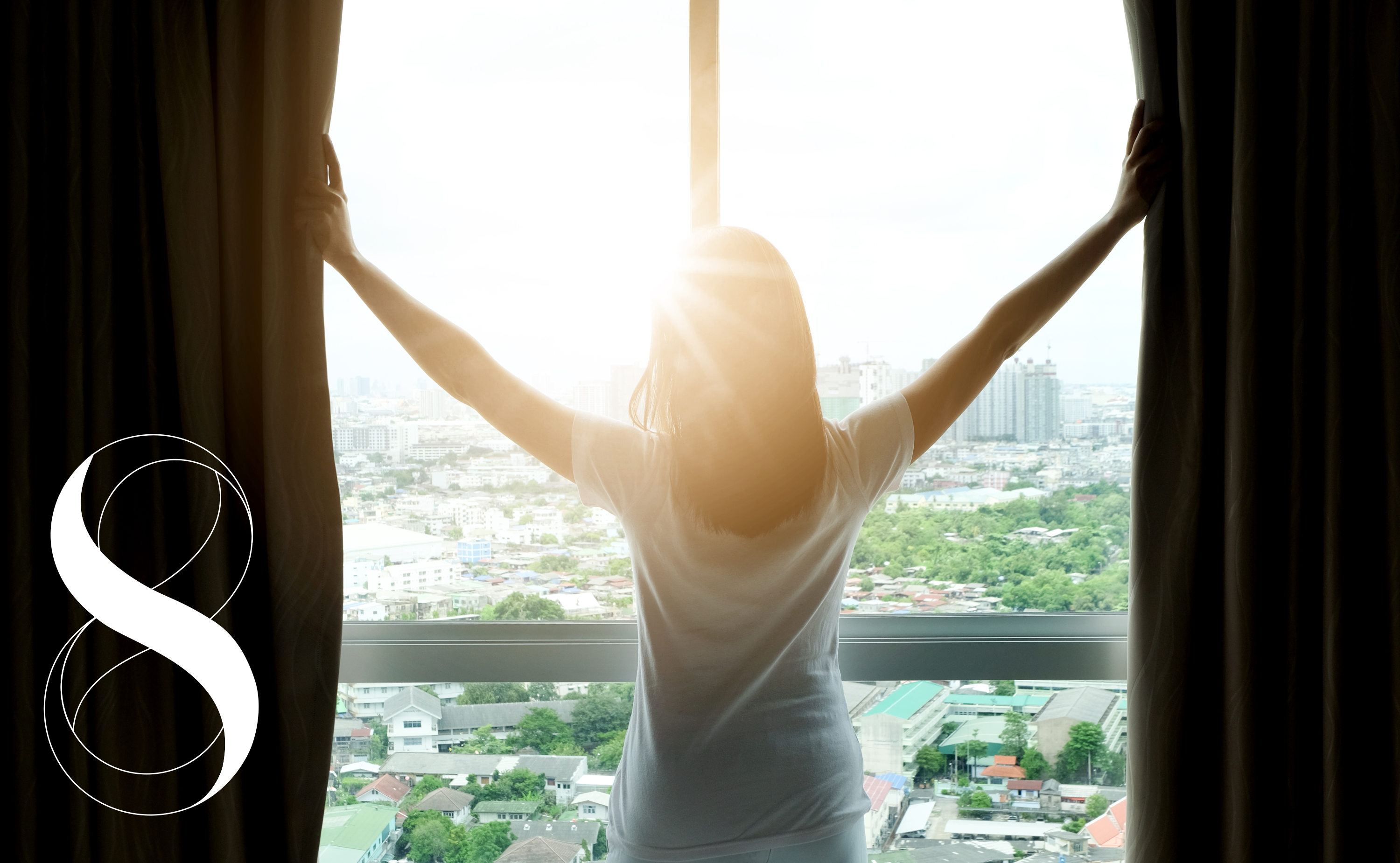 Eine Frau schließt die Vorhänge, sie blickt aus einem Fenster mit Blick auf eine Stadtlandschaft, über der die Sonne untergeht. Ein Symbolfoto mit dem 8-Elements-Health-Logo von Life Light links im Bild für erholsame Nächte trotz Hitze.