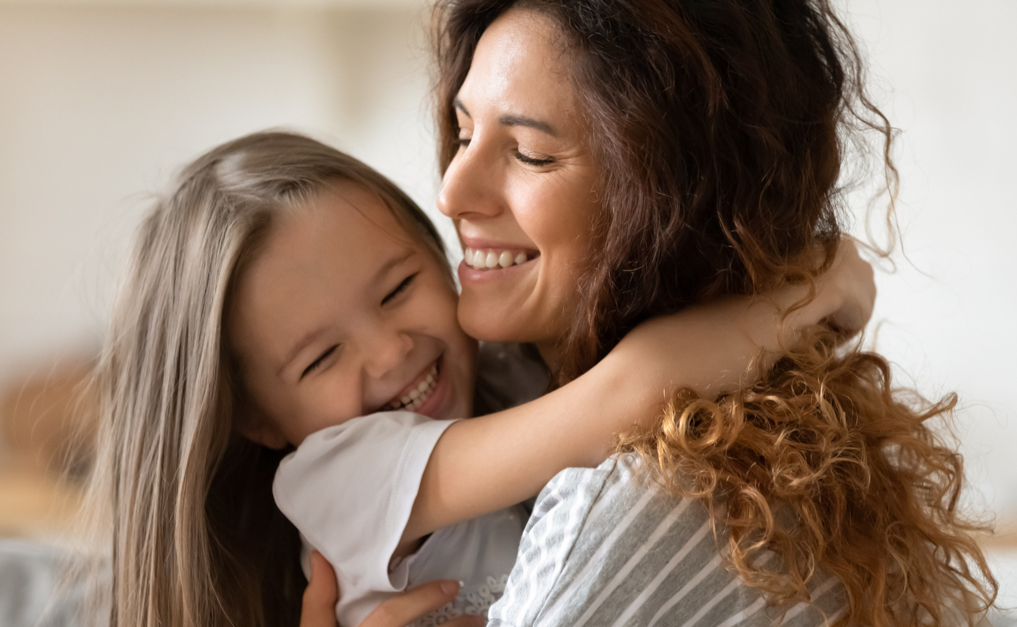 Eine Frau umarmt lächelnd ein Kind, das ebenfalls lächelt und die Augen geschlossen hat. Ein Symbolfoto für ein gesundes Kind mit einem starken Immunsystem.