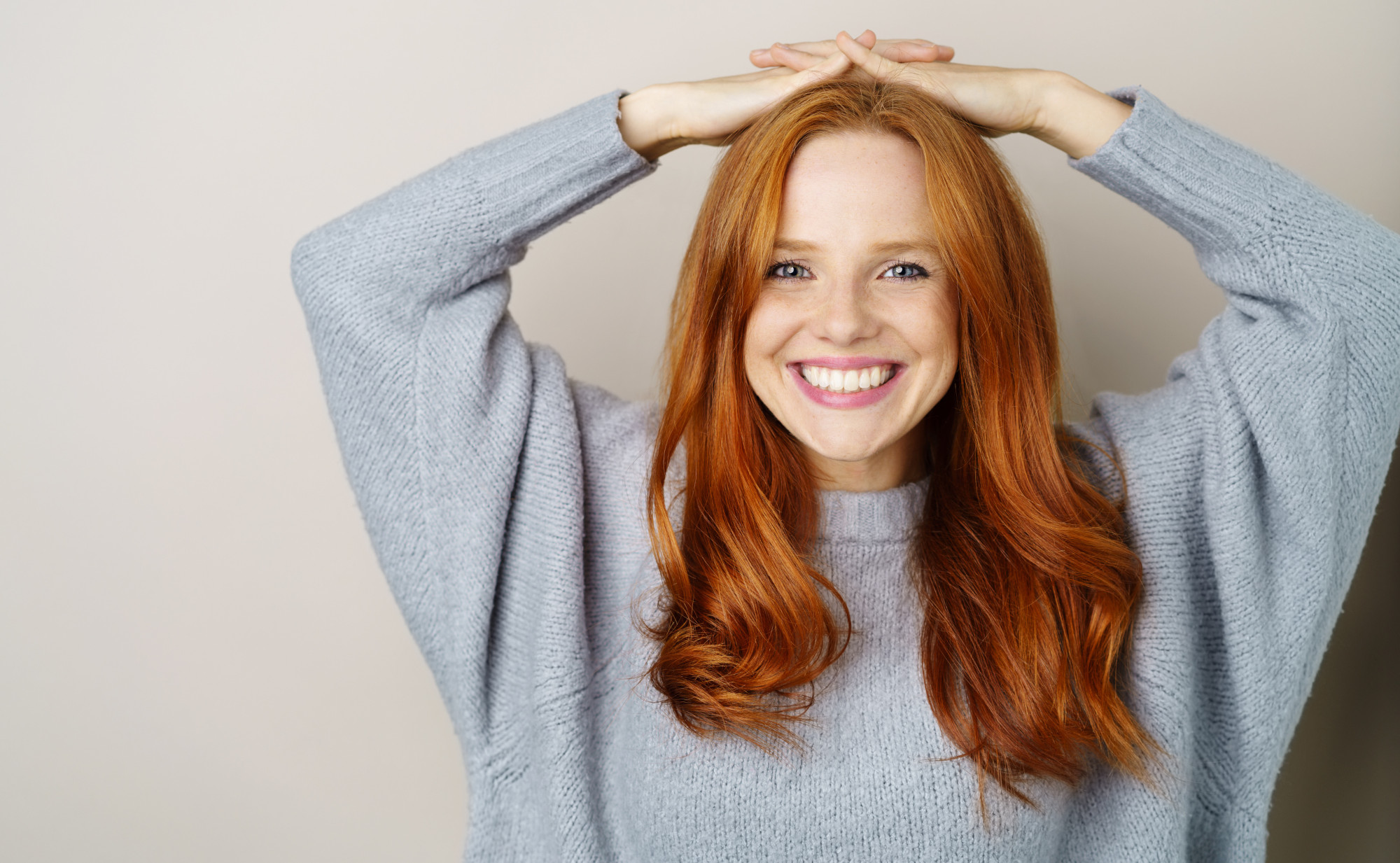 Eine lächelnde Frau mit roten Haaren und Sommersprossen schaut direkt in die Kamera, die Hände auf dem Kopf verschränkt. Ein Symbolfoto für gesunde Venen im menschlichen Körper.